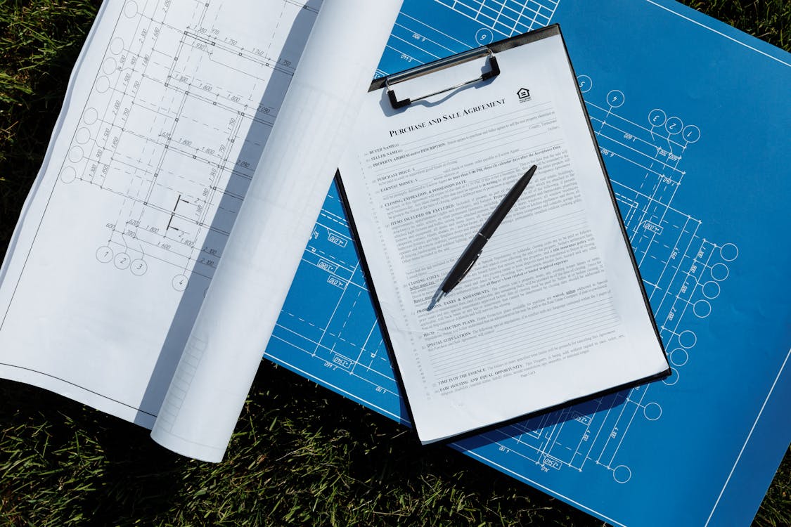 Purchase agreement document on a clipboard resting on top of blue construction blueprints