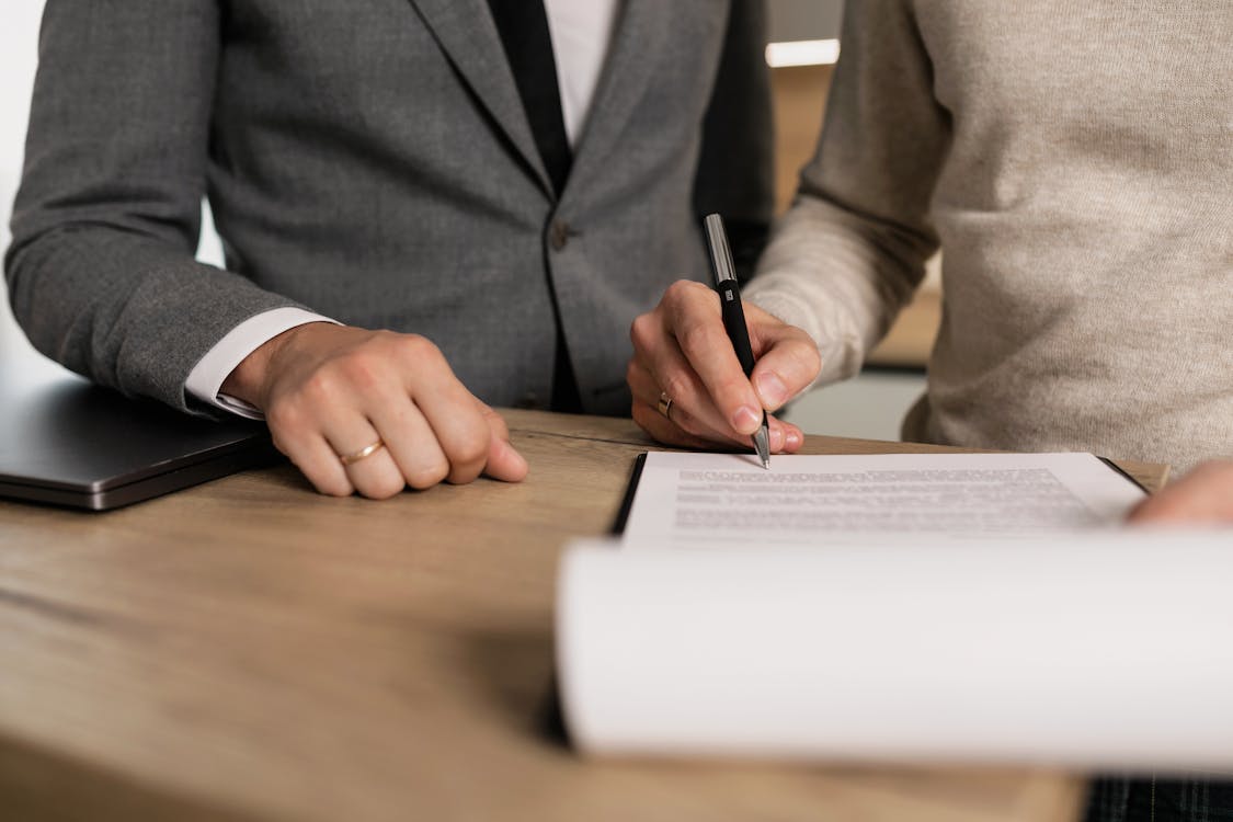 Two professionals at a wooden desk signing a legal contract document with a pen