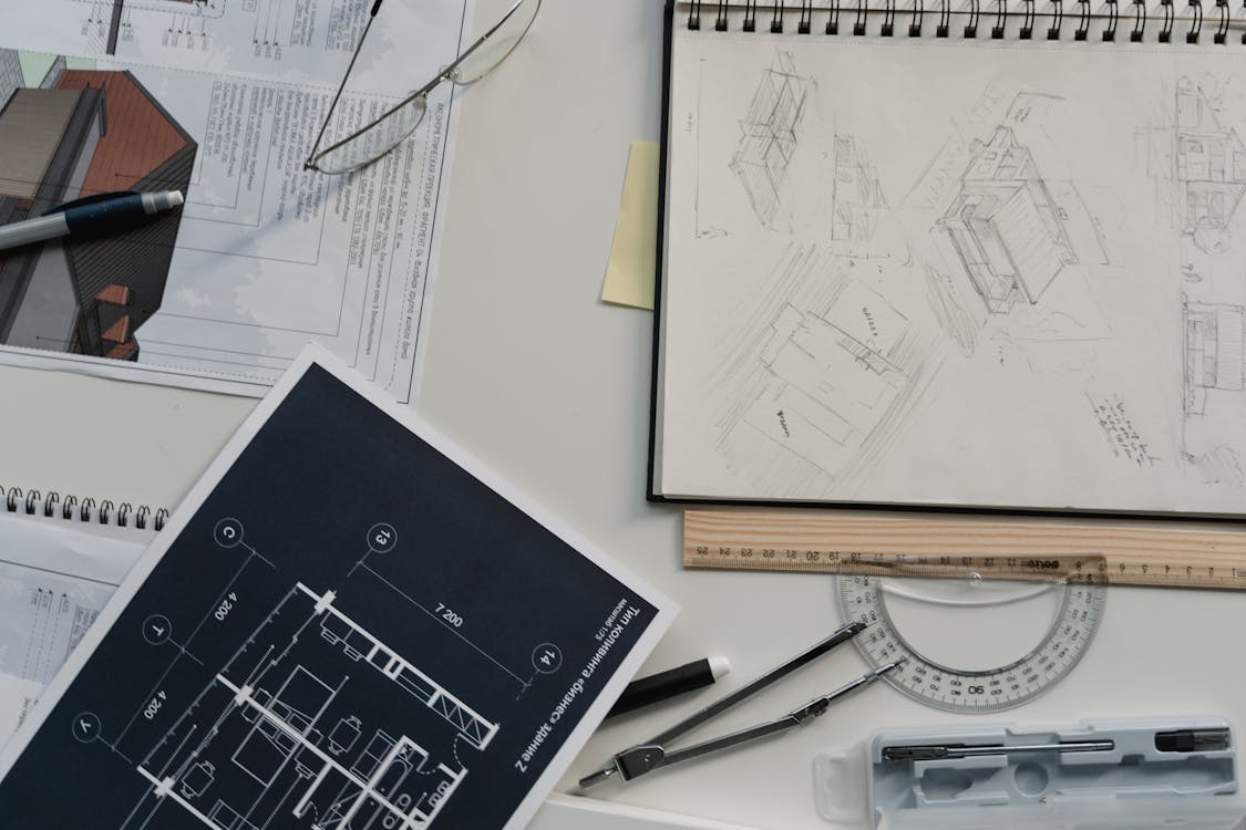 Architect workspace with floor plans, sketches, compass, protractor, and drawing tools on a desk
