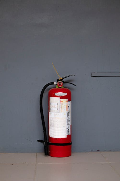 Red fire extinguisher mounted on a gray wall with inspection labels visible
