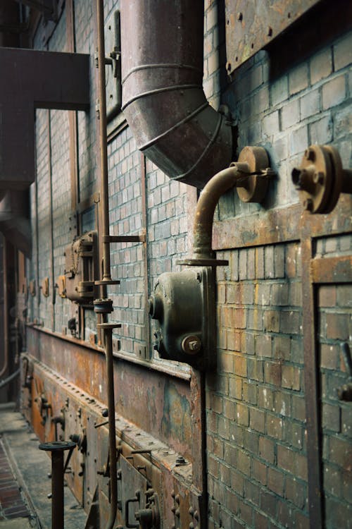 Old industrial building interior with rusted pipes, valves, and brick walls
