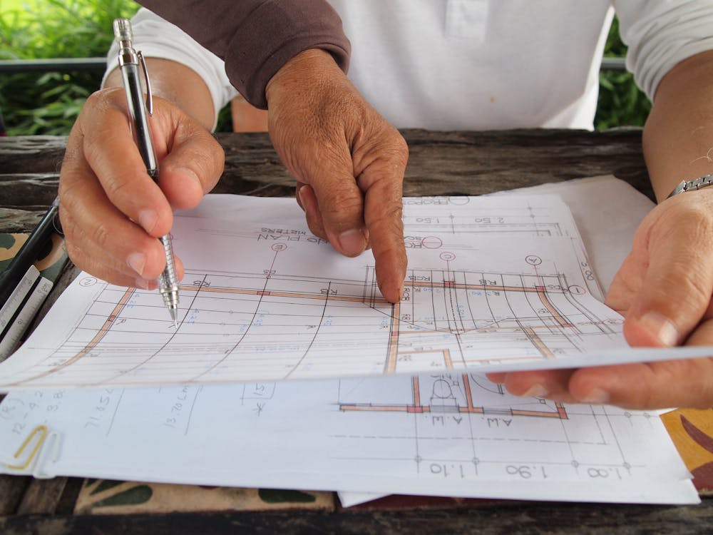 Hands pointing at a detailed architectural blueprint with dimensions and handwritten annotations