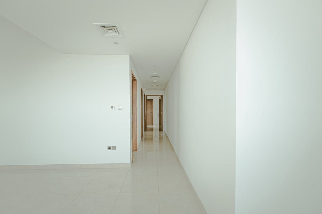 Clean empty building corridor with white walls and tile flooring before renovation begins