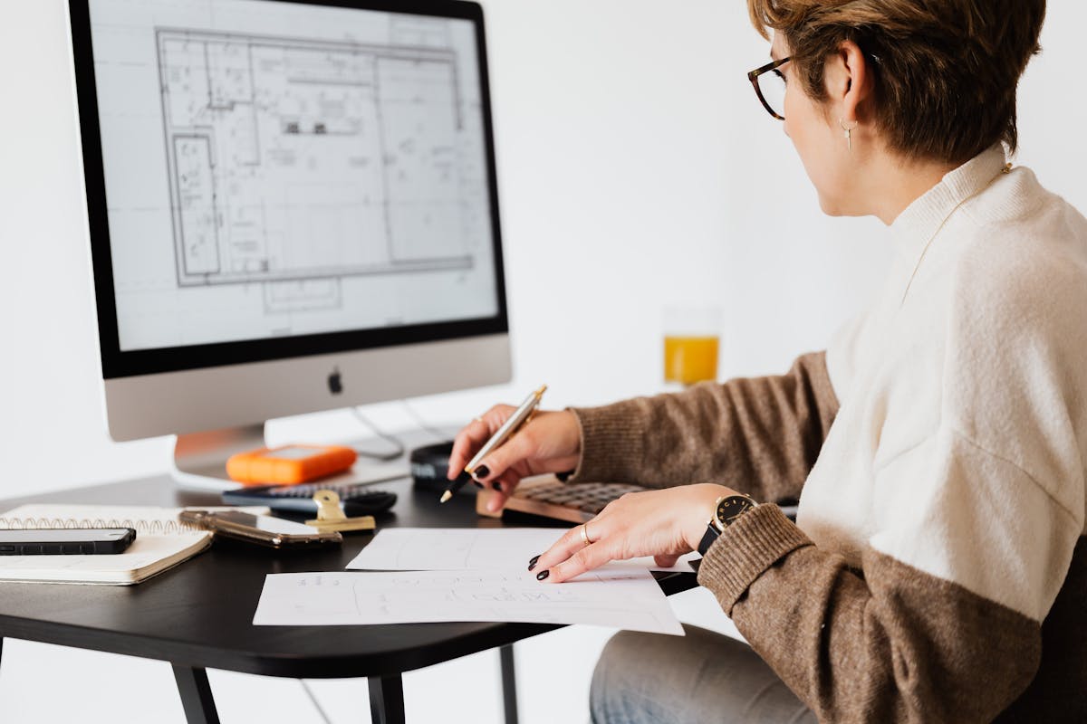 Person working at a desk with architectural floor plans displayed on a computer monitor and printed sheets
