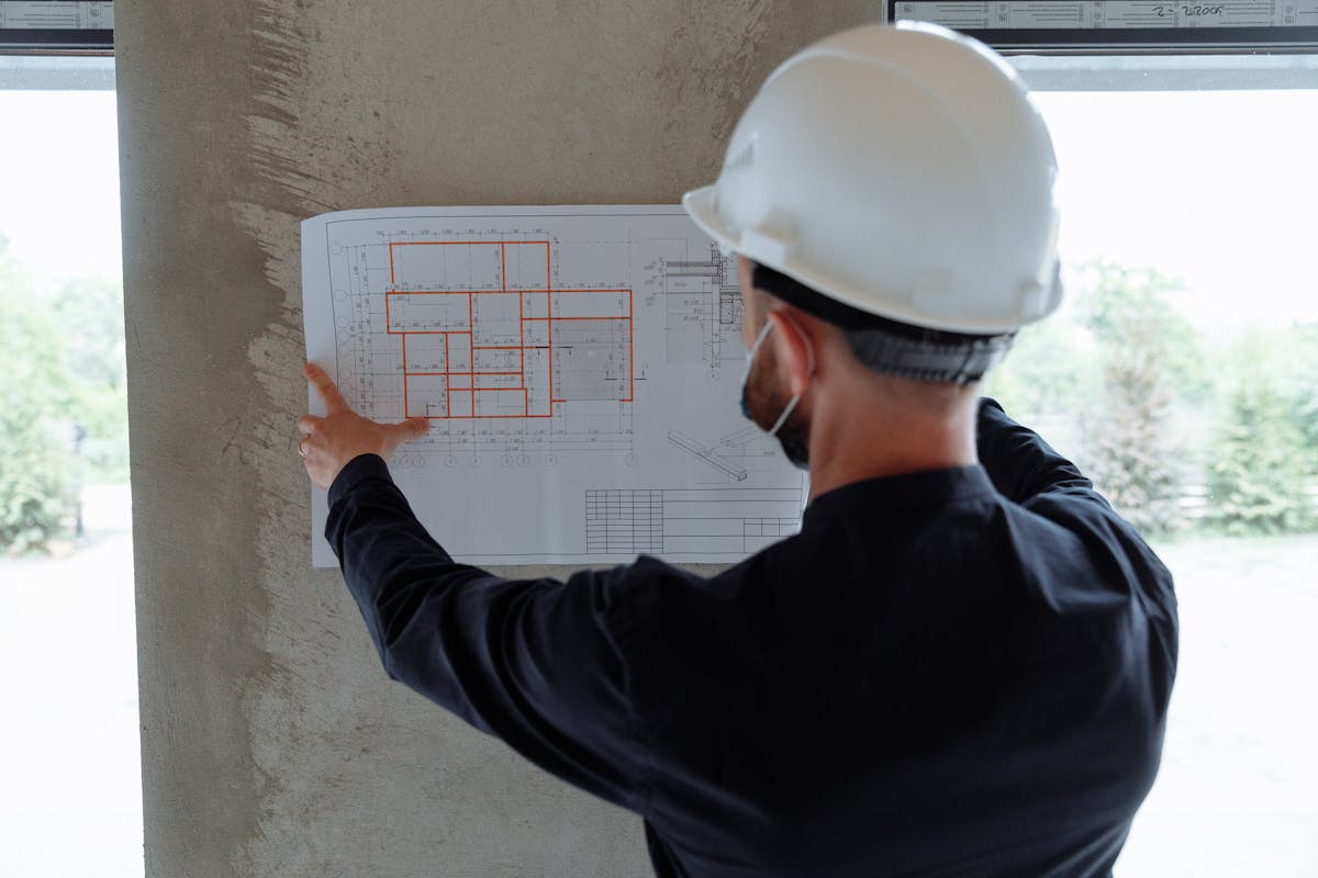 Engineer reviewing architectural floor plans with construction hardhat and measuring tools