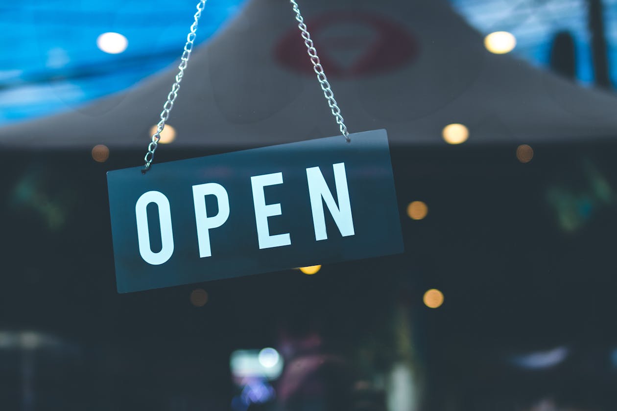 Open sign hanging on a local business storefront glass door with warm bokeh lights in the background