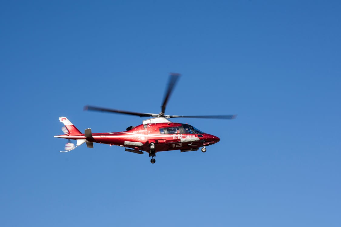 Red helicopter in flight against clear blue sky, representative of manned aircraft used for aerial LiDAR surveys