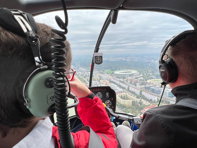 Two pilots wearing headphones in a helicopter cockpit flying over a city