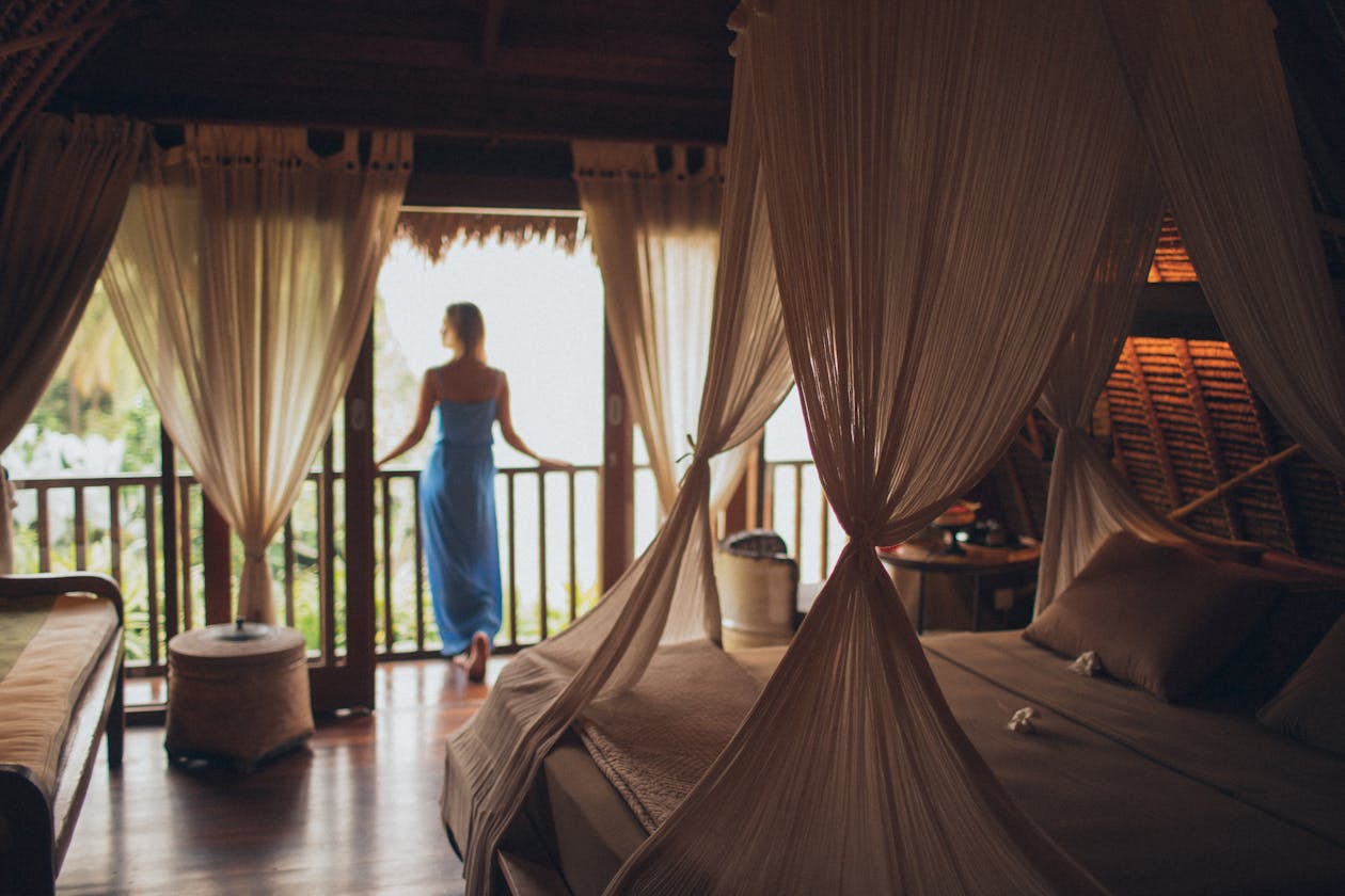 Luxury resort hotel room with canopy bed and sheer curtains, guest looking out at tropical landscape from balcony — hospitality properties use virtual tours to showcase rooms and build booking confidence
