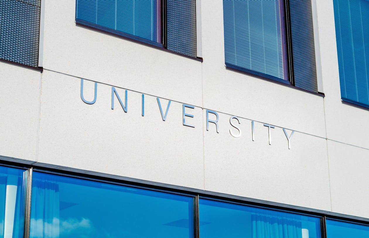 Modern university building facade with "UNIVERSITY" lettering and blue-tinted glass windows — educational institutions use virtual tours for remote campus visits and student recruitment