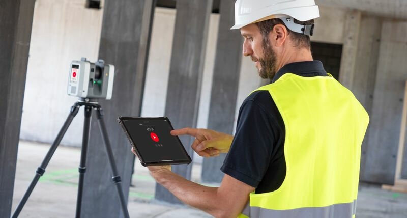 Technician in safety vest and hard hat operating a Leica RTC360 3D laser scanner via tablet inside a building under construction