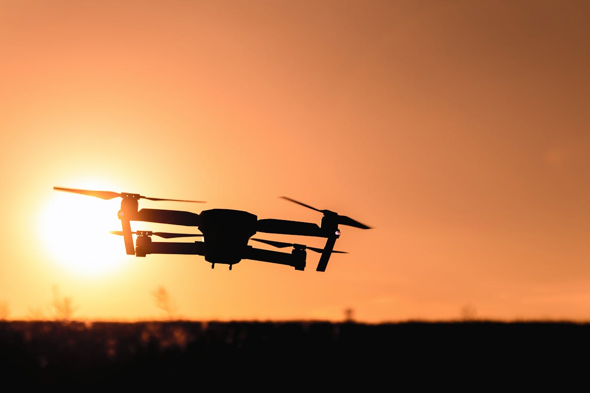 Drone silhouetted against an orange sunset sky during an aerial LiDAR survey mission