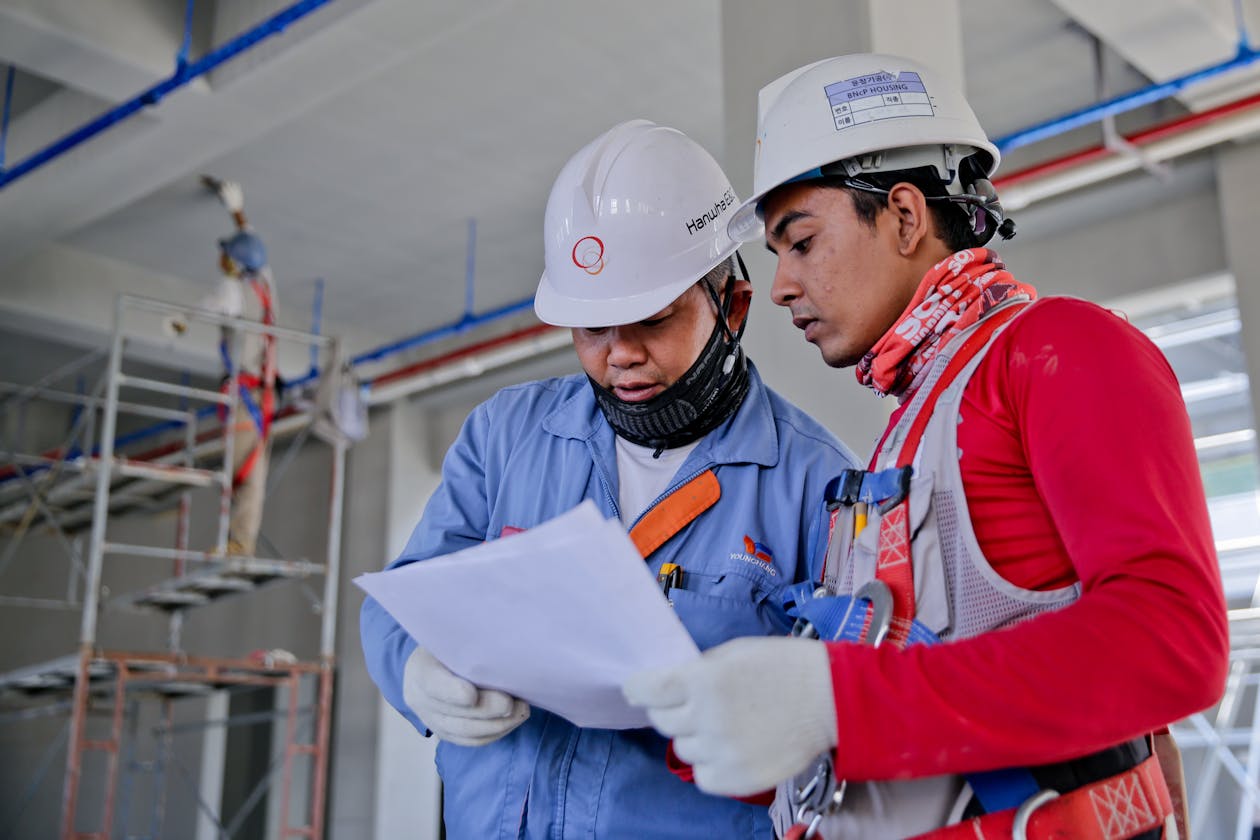 Two construction workers in hard hats reviewing building plans at a construction site with scaffolding — progress documentation is a key AEC application where Matterport visual tours add value