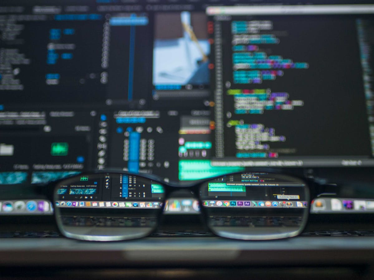 Glasses resting in front of multiple monitors displaying code and software applications