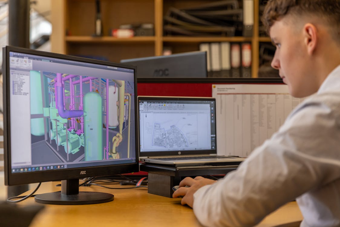Engineer reviewing a colorized 3D BIM model with MEP systems on dual monitors showing scan-to-BIM workflow output