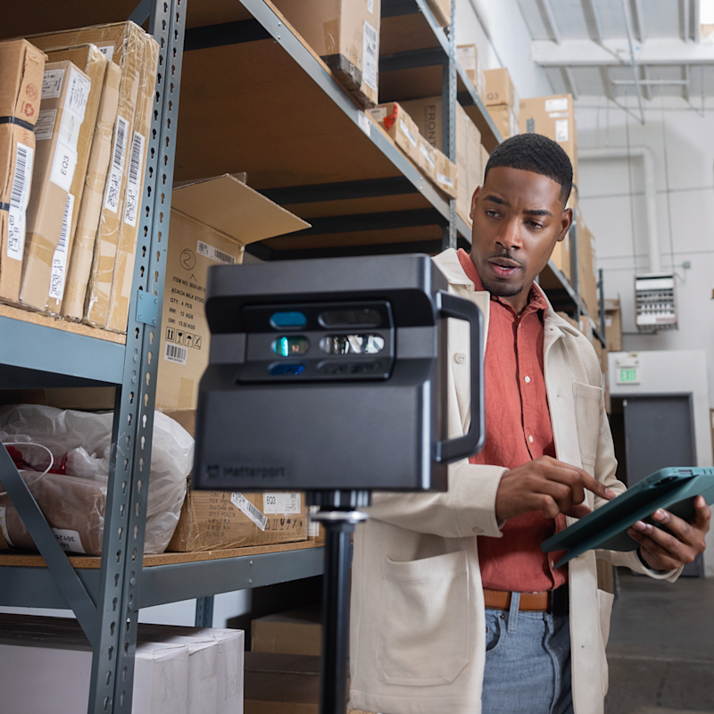 Technician using a Matterport Pro2 camera to scan a warehouse while reviewing data on a tablet