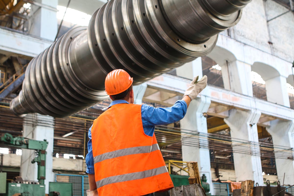Industrial worker in safety vest and hard hat inspecting heavy machinery in a manufacturing facility