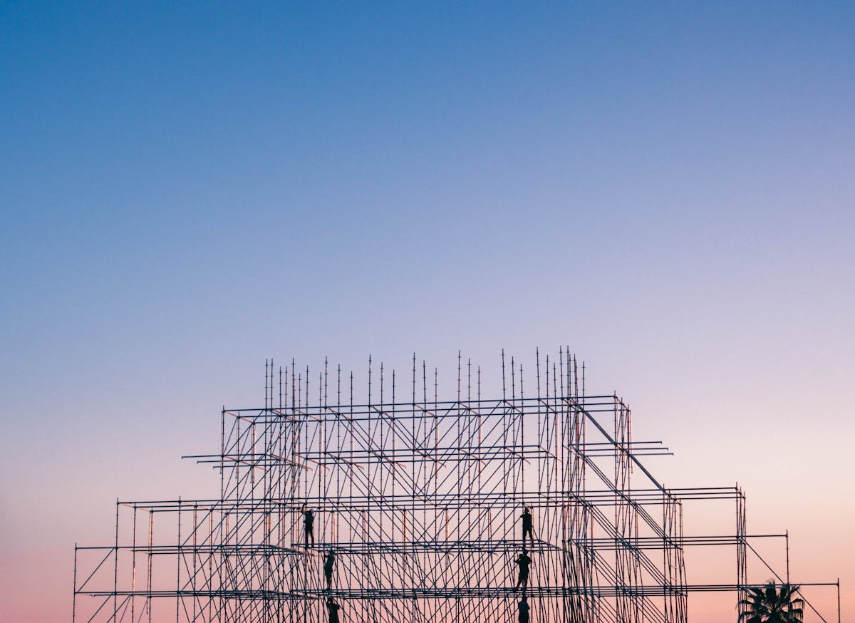 Construction scaffolding silhouetted against a gradient sunset sky showing building structure framework