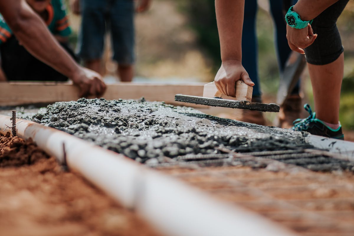 Workers leveling and smoothing wet concrete at a construction site foundation