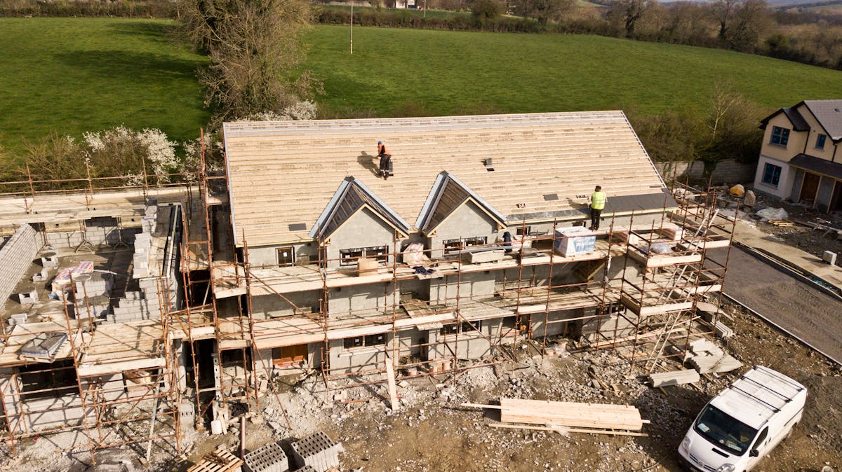 Aerial view of a building under construction with workers on the roof and scaffolding