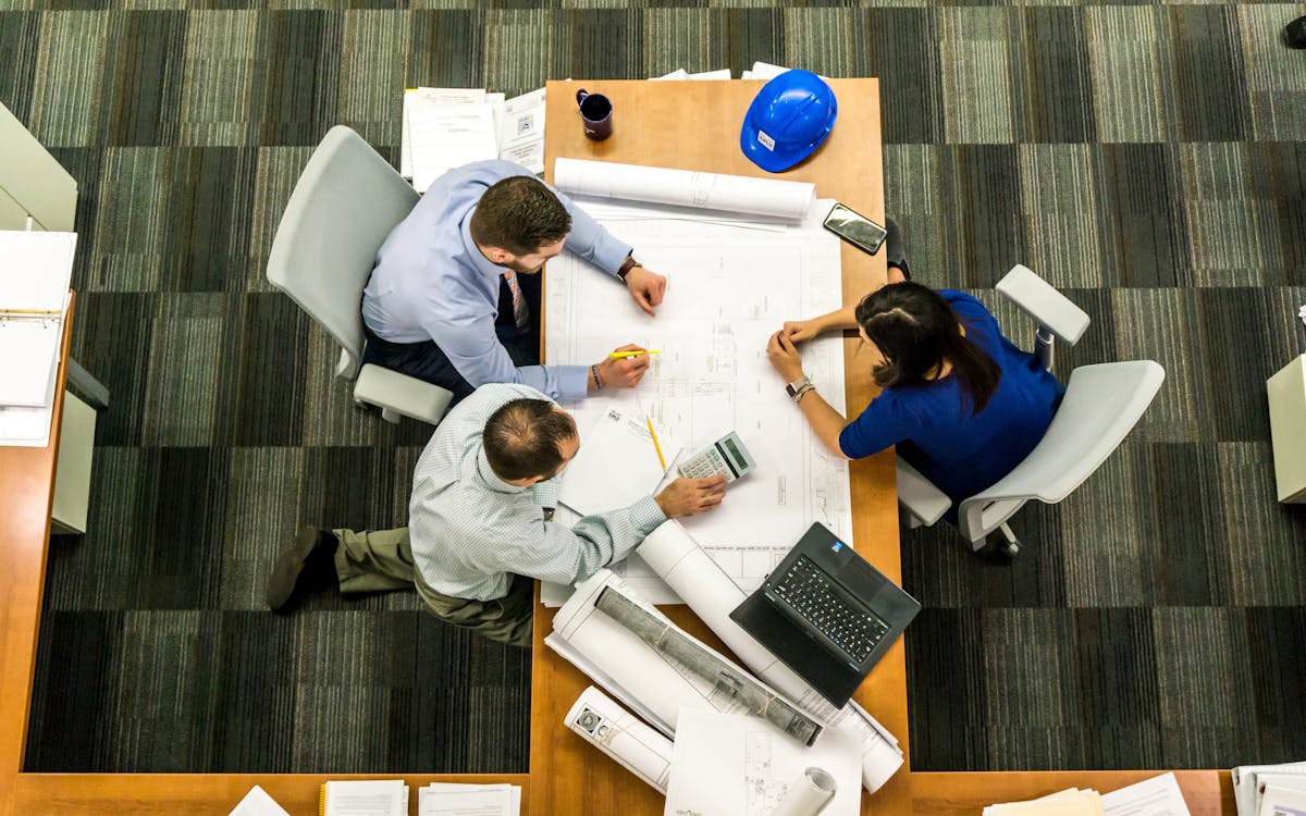 Overhead view of a team of professionals reviewing construction plans with blueprints, laptop, and hardhat