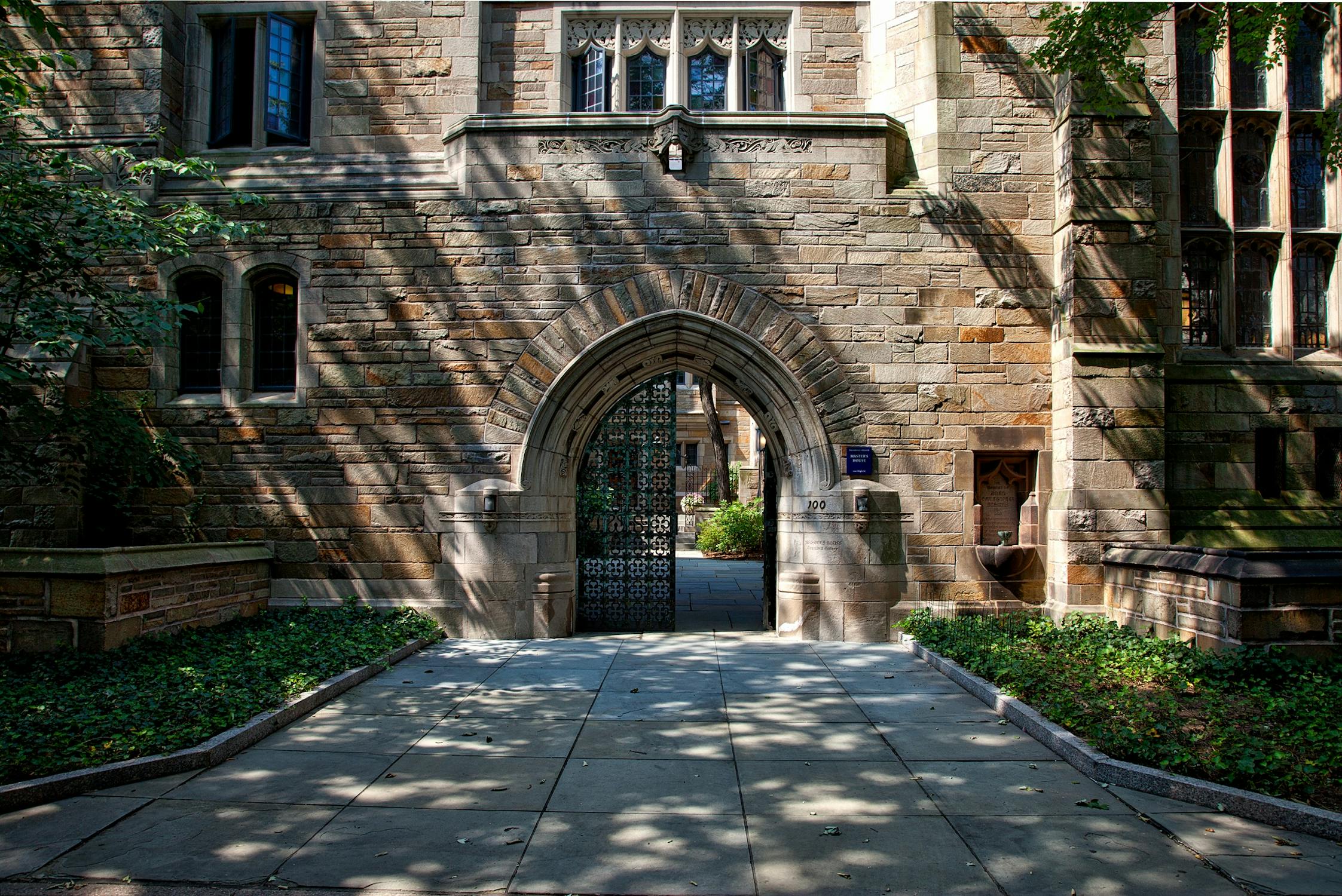 Gothic stone archway entrance on a university campus with tree-lined walkway